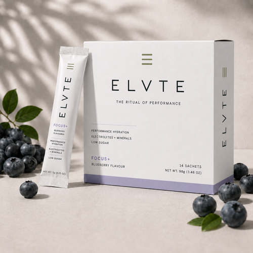 ELVTE Focus+ Blueberry Flavour performance hydration sachets shown with a white and lavender box and one individual sachet, styled with blueberries and leaves on a neutral beige surface.