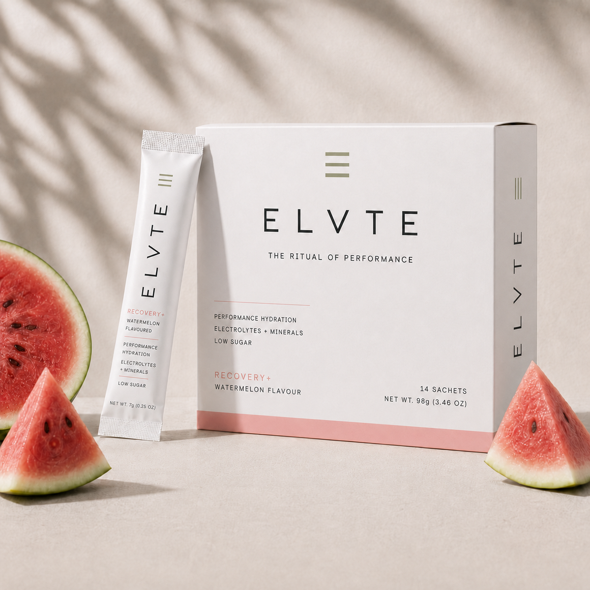ELVTE Recovery Watermelon Flavour electrolyte sachets shown with a white and pink product box, a single packet, and watermelon slices on a beige surface with soft leaf shadows.